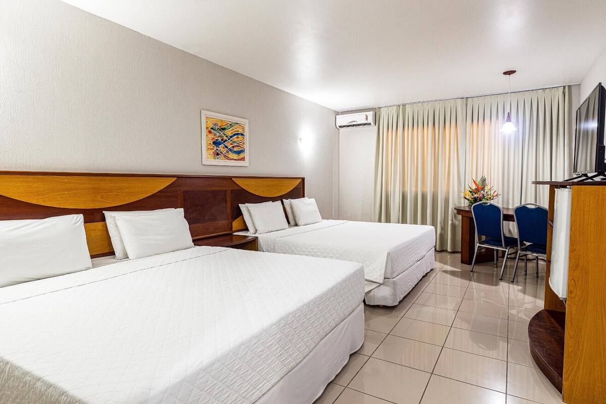 A hotel room with two beds, a desk, a chair, a television, and a painting on the wall.