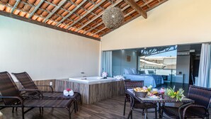 A spacious balcony with wicker furniture, a central table with breakfast items, and a view of a building through glass doors. - Nauticomar Resort All Inclusive & Beach Club (Porto Seguro)