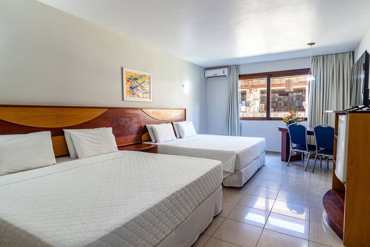A hotel room with two beds, a desk, a chair, a TV, and a window with curtains.