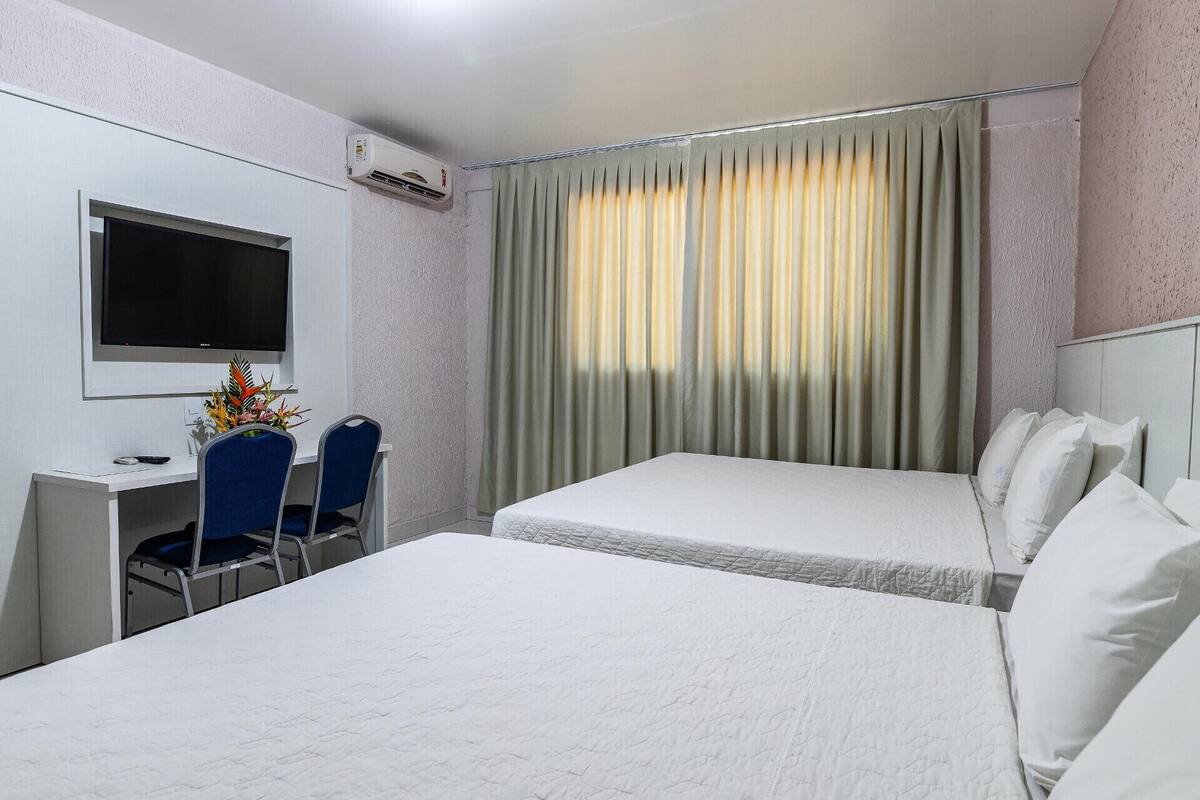 A hotel room with two beds, a desk with a chair, a flat-screen TV, and a window with curtains.