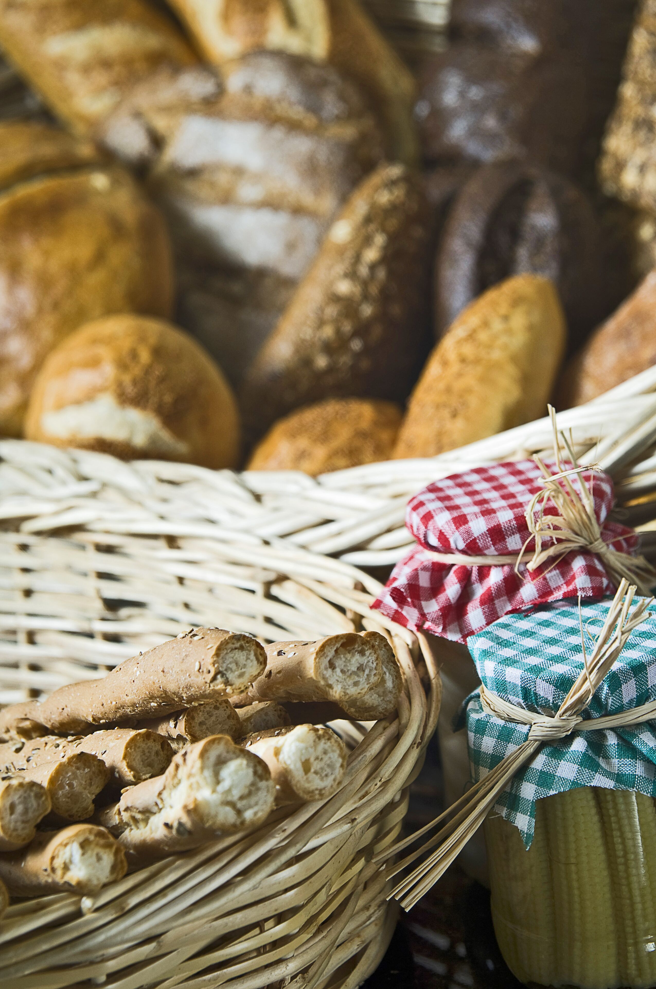 Un panier rempli de différents types de pain, notamment des baguettes et des petits pains, et décoré de serviettes à carreaux.