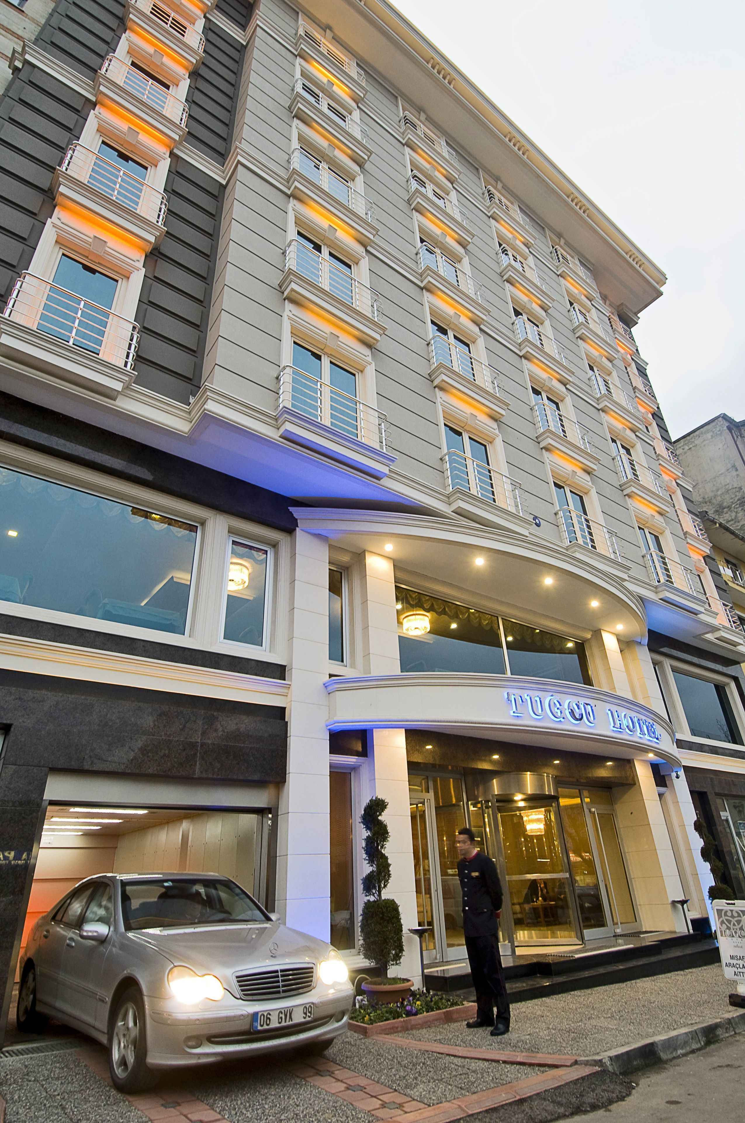 A hotel entrance with a car parked in front, a concierge, and a sign reading "Tugboat Hotel".