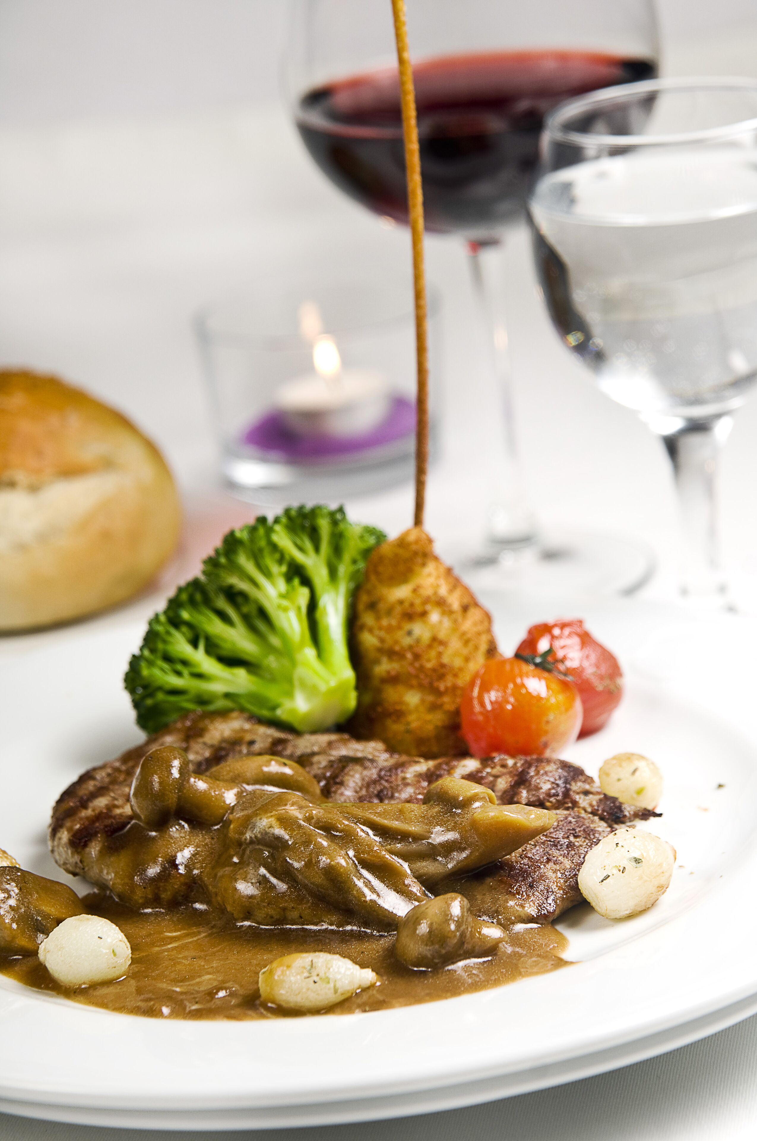 Plat de menjar amb entrecot, bolets, bròcoli i tomàquets cherry, acompanyat d'un got de vi negre i un got d'aigua.