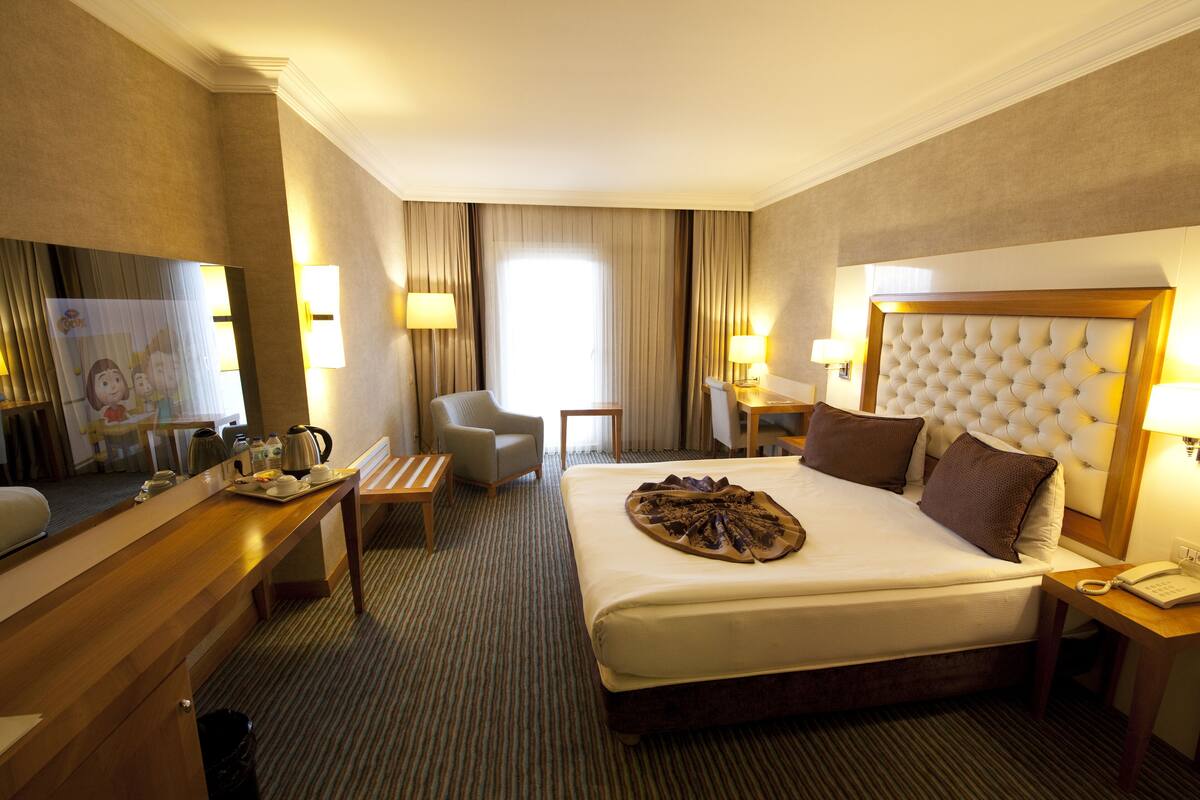 A hotel room with a large bed, a desk with a chair, a small table, and a television.