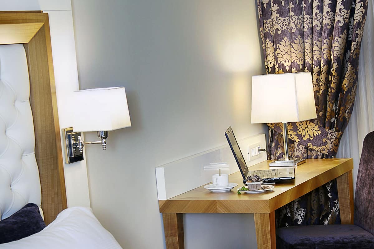 A hotel room with a bed, a desk with a laptop, a chair, and a lamp.