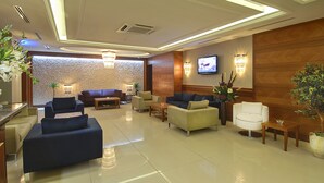 A modern hotel lobby with a mix of sofas and armchairs, a flat-screen TV mounted on the wall, and a reception desk. - Tugcu Hotel Select (Bursa)