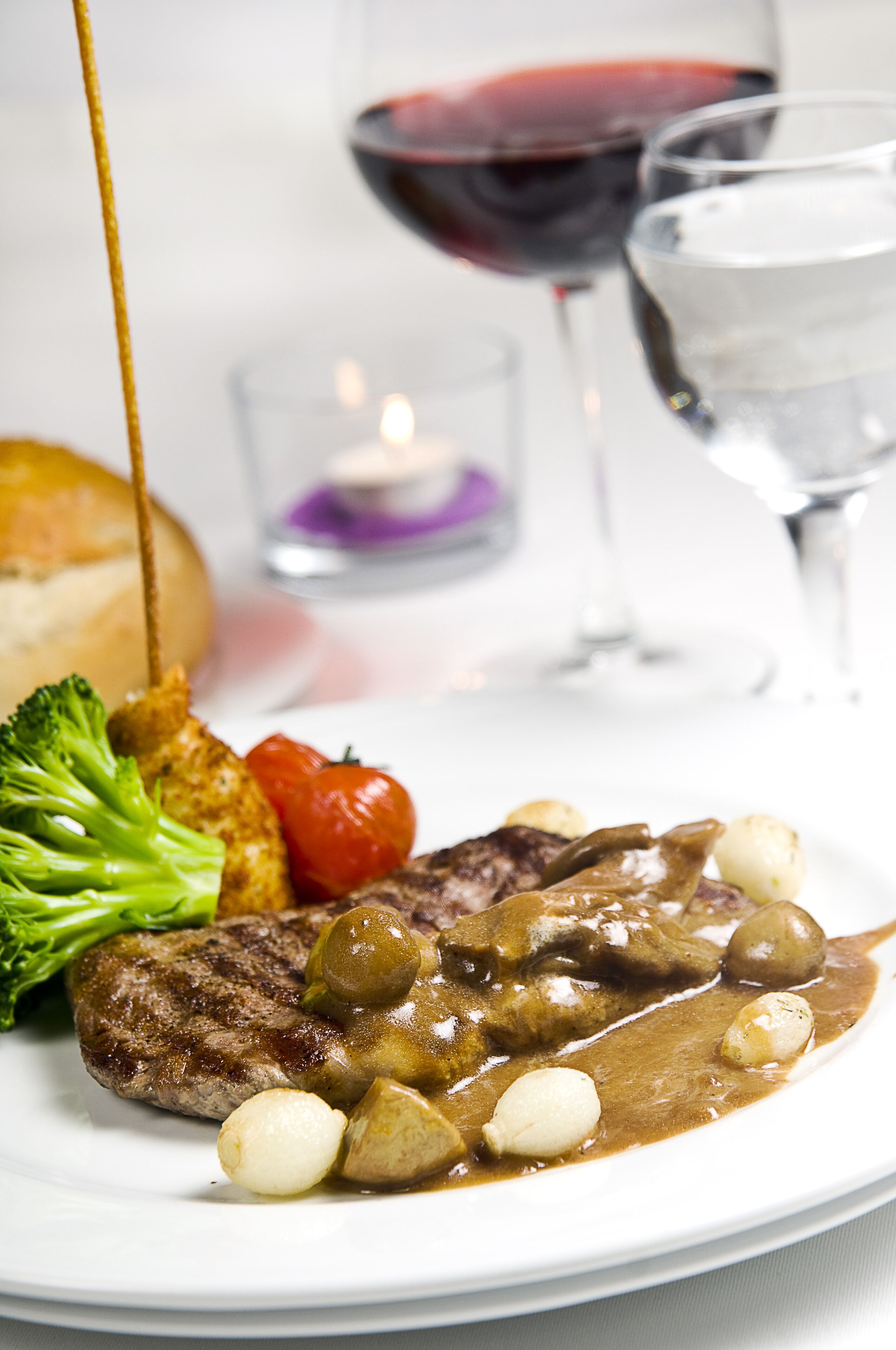 A plate of food with steak, vegetables, and sauce, accompanied by a glass of red wine and a glass of water.