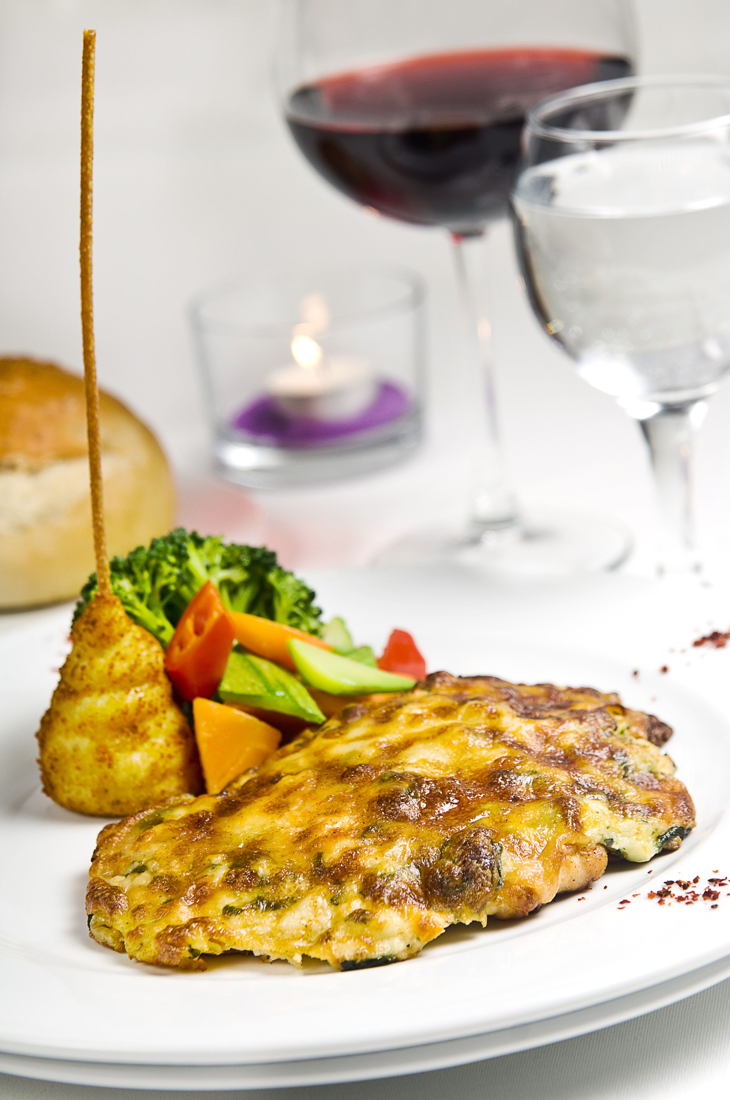 A plate with a grilled chicken breast, vegetables, and a bread roll.