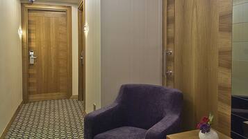 A hallway with patterned carpet, a purple armchair, a small wooden table with a vase, and a wooden wardrobe.