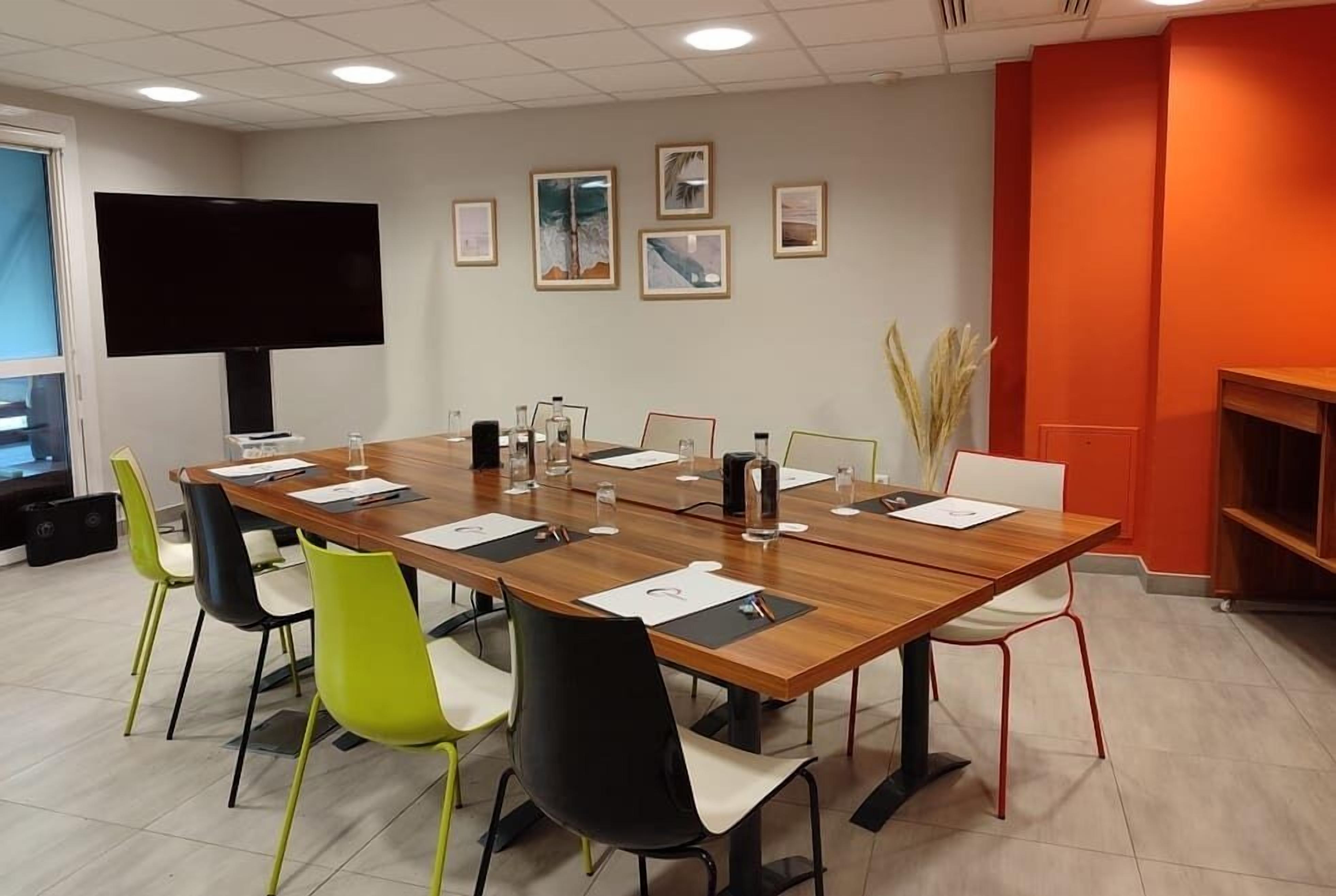 A conference room with a long table, chairs, a TV, framed pictures on the wall, and a bookshelf.