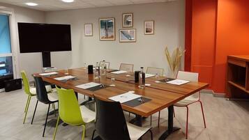 A conference room with a long table, chairs, a TV, framed pictures on the wall, and a bookshelf.