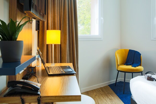 Una habitación de hotel con escritorio de madera, una computadora portátil, teléfono, lámpara, silla y cama.