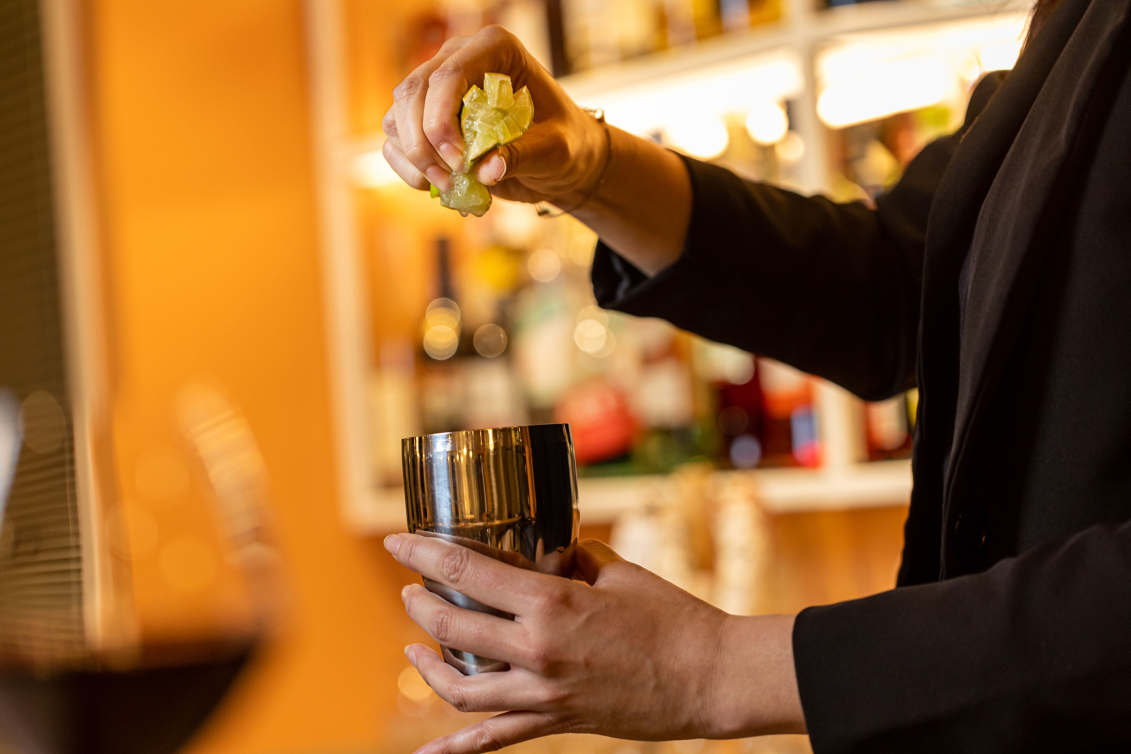 A person holding a metallic cup and a piece of fruit, likely preparing a drink.