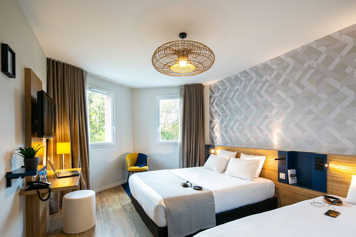 A modern hotel room with a large bed, a desk with a laptop, a chair, and a television.