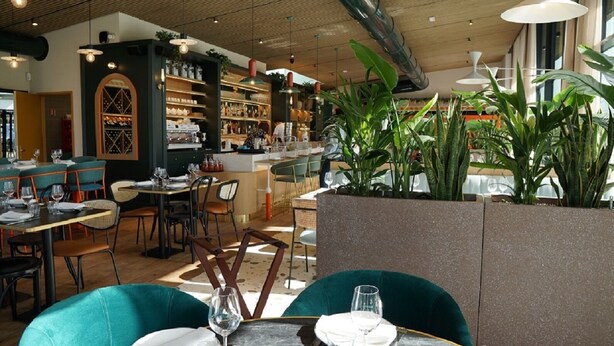 Un restaurante con sillas color turquesa, una alacena para vinos y una zona de bar.