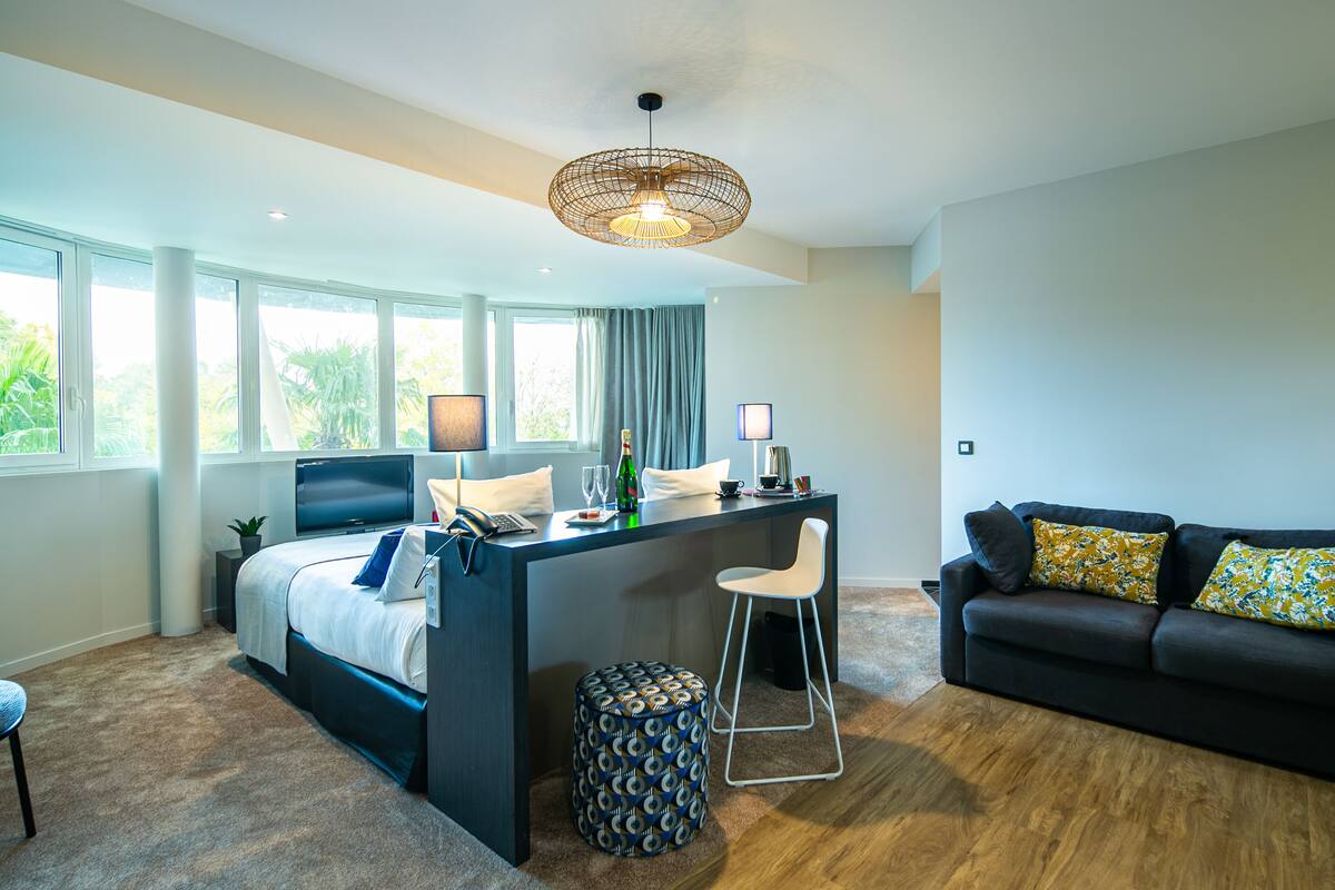 A modern bedroom with a bed, a desk, a sofa, and a large window.