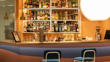 Zona de bar con estantes llenos de botellas de licor, dos sillas azules y una máquina de café.