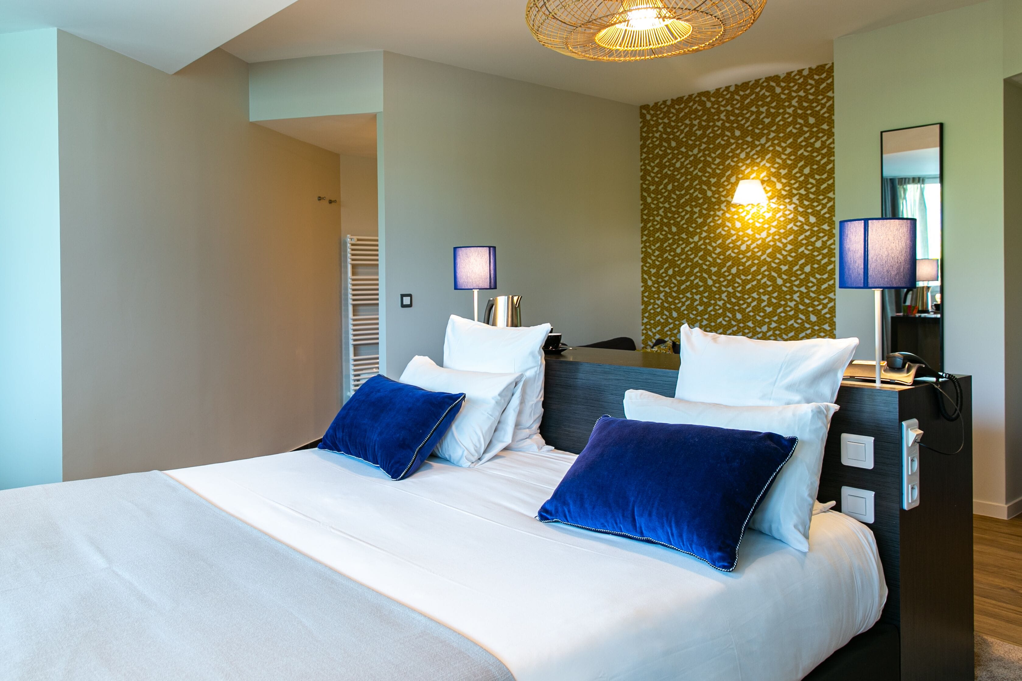 A modern hotel room with a large bed, two bedside lamps, a mirror, and a wall with a leafy pattern.