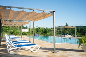 Un área junto a la piscina con sillones de descanso y una sombrilla.