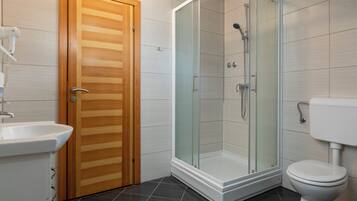 Un baño moderno con puerta de madera, cabina de ducha con paredes de vidrio, lavamanos blanco y un inodoro.