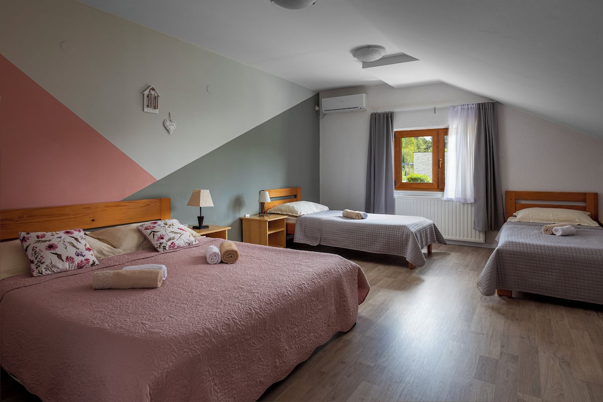 A hotel room with two single beds, a wooden headboard, a nightstand, a lamp, and a window with curtains.