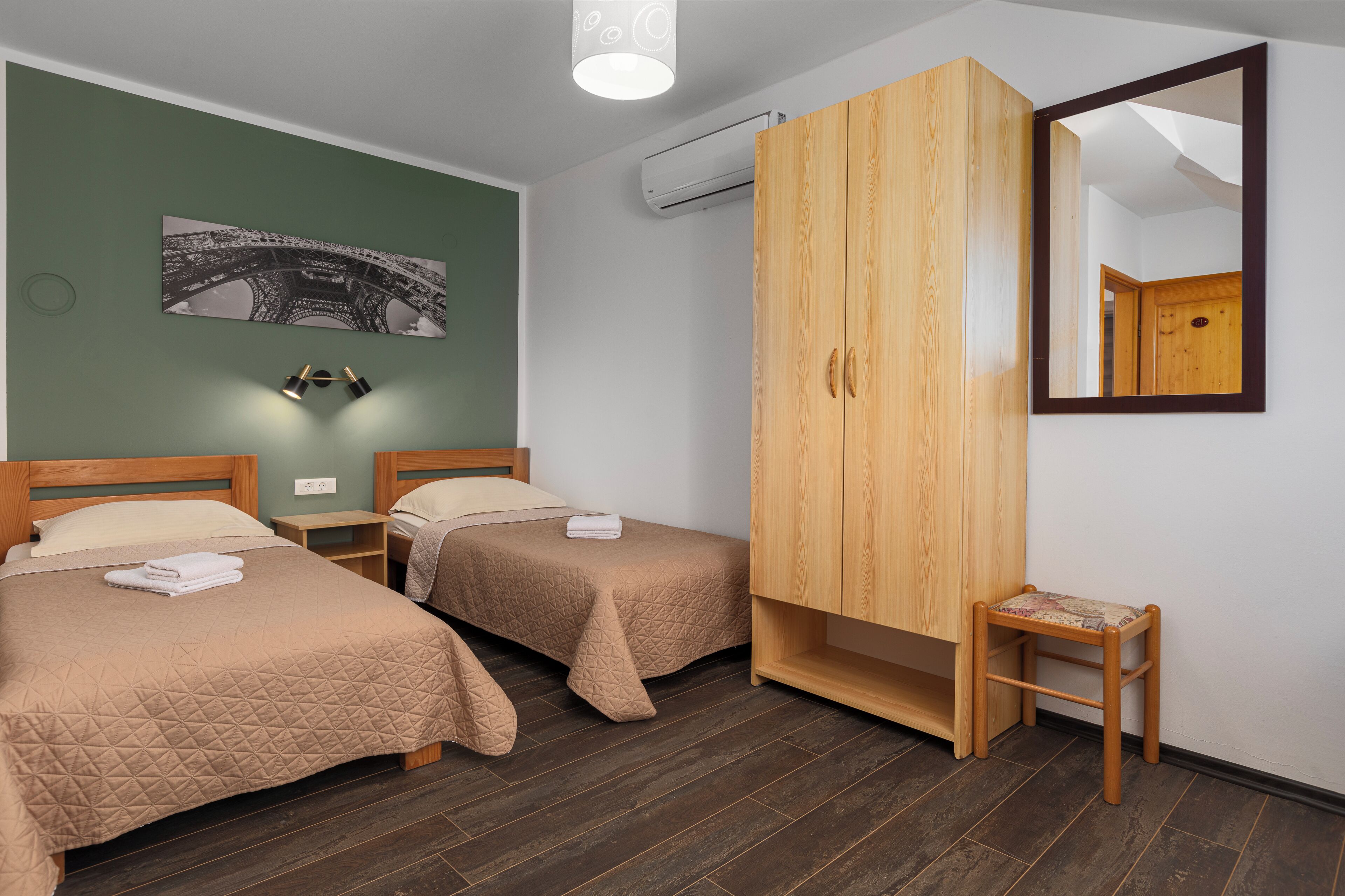 A hotel room with two beds, a wardrobe, a small stool, and a wall-mounted air conditioning unit.