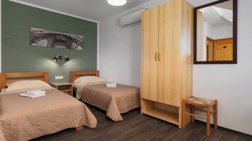 A hotel room with two beds, a wardrobe, a small stool, and a wall-mounted air conditioning unit.