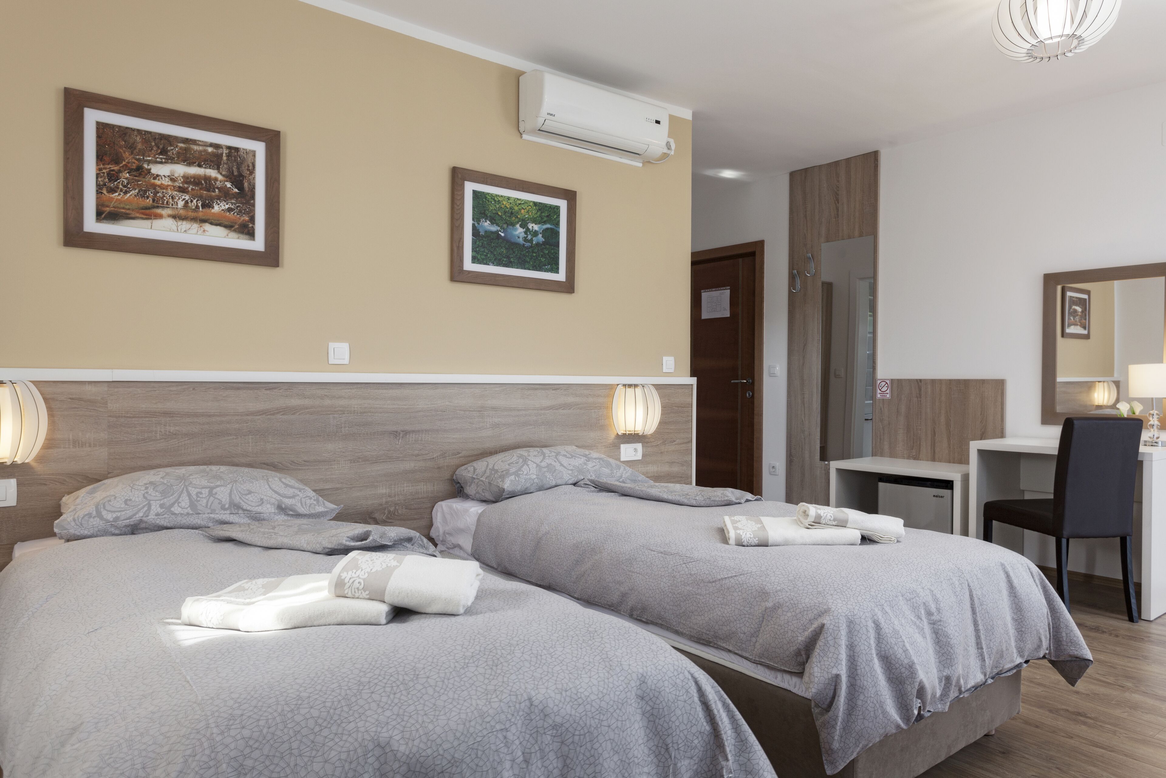 Ett hotellrum med två sängar, ett skrivbord, en stol och en spegel.