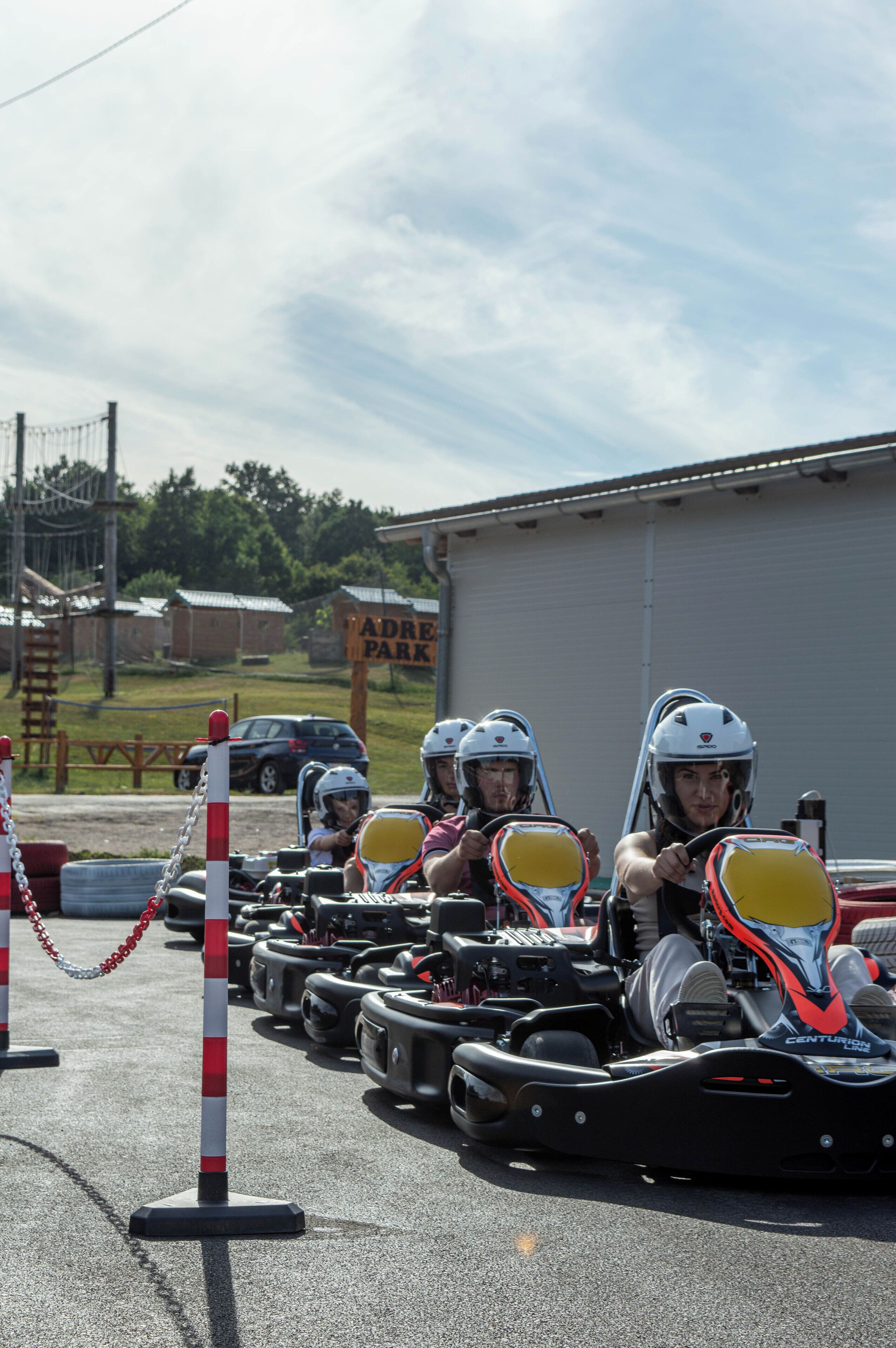 A go-kart track with multiple go-karts and drivers in helmets, a sign for 'Padre Park', and a building in the background.