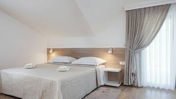 A modern hotel room with a large bed, a bedside table, a nightstand, and a window with curtains.