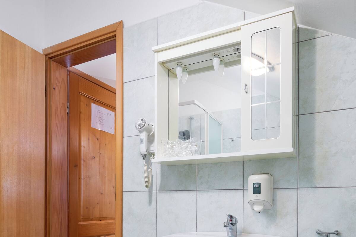 A bathroom with a wooden door, a white sink, a mirror, and a handheld hair dryer.