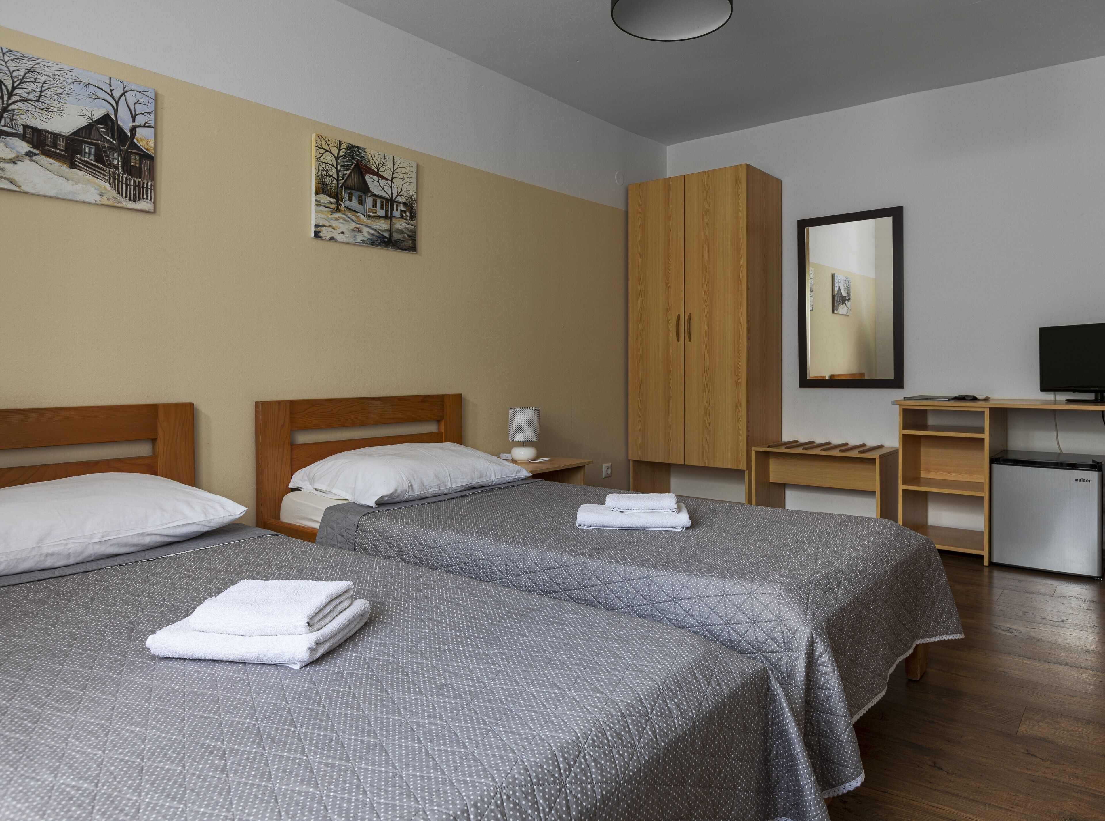 Ein Hotelzimmer mit zwei Betten, einem Holzschrank, einem Schreibtisch mit Fernseher und Bildern an den Wänden.
