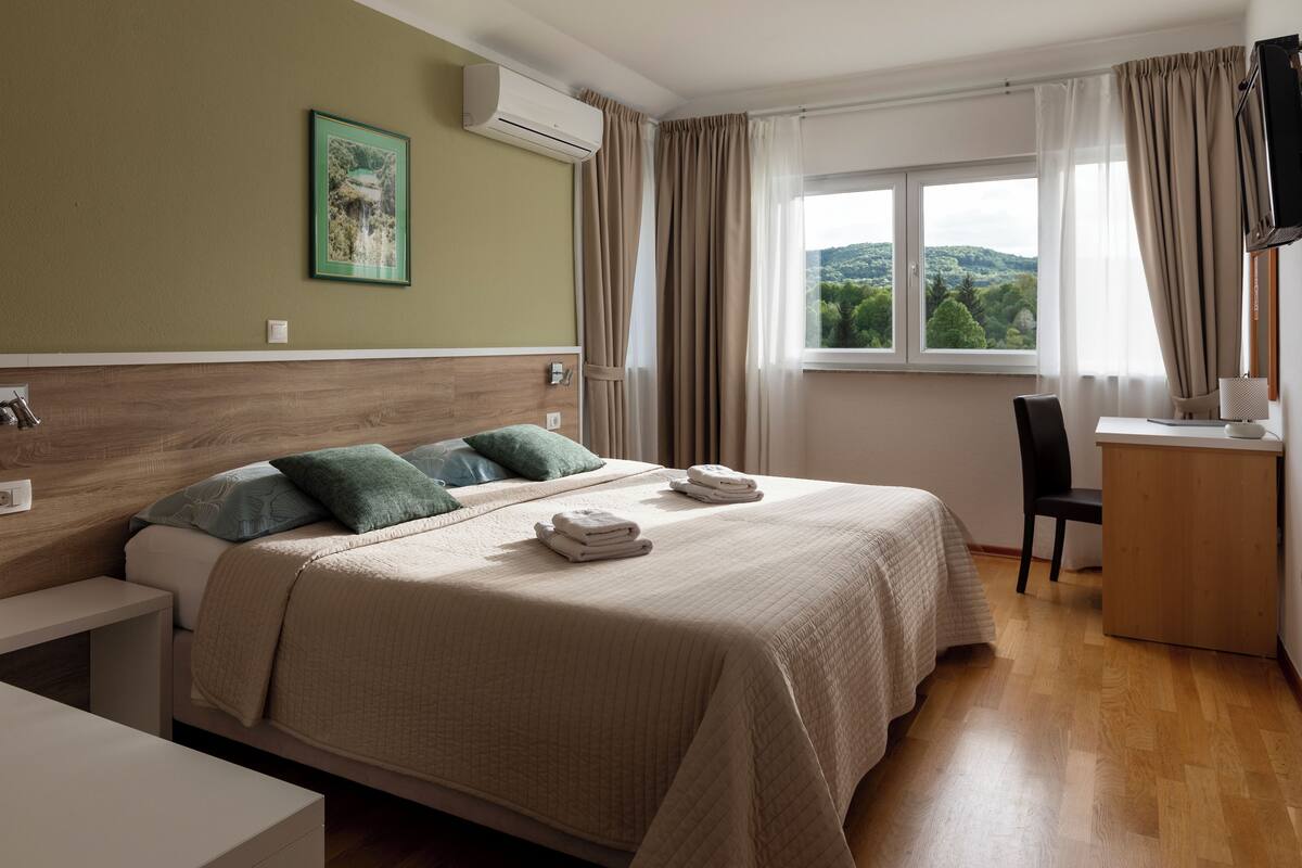 A hotel room with a bed, a desk, a chair, a TV, and a window with curtains.