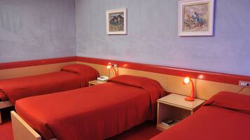 Habitación de hotel con dos camas individuales, cada una con una colcha roja y una mesita de noche con lámpara. Se observan dos cuadros en la pared.