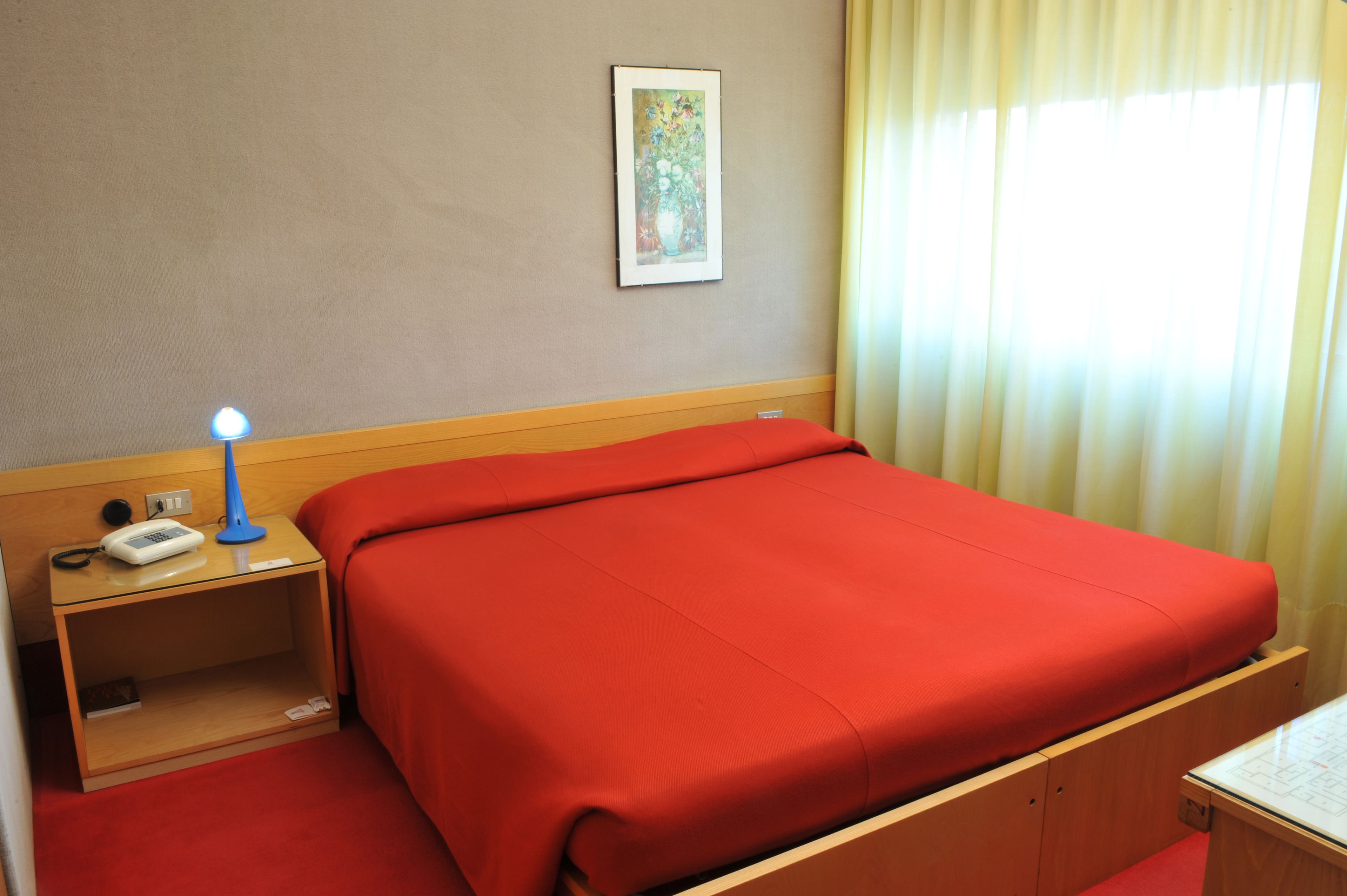 Habitación de hotel con una cama individual, una mesita de noche con lámpara, un teléfono y un cuadro enmarcado en la pared.