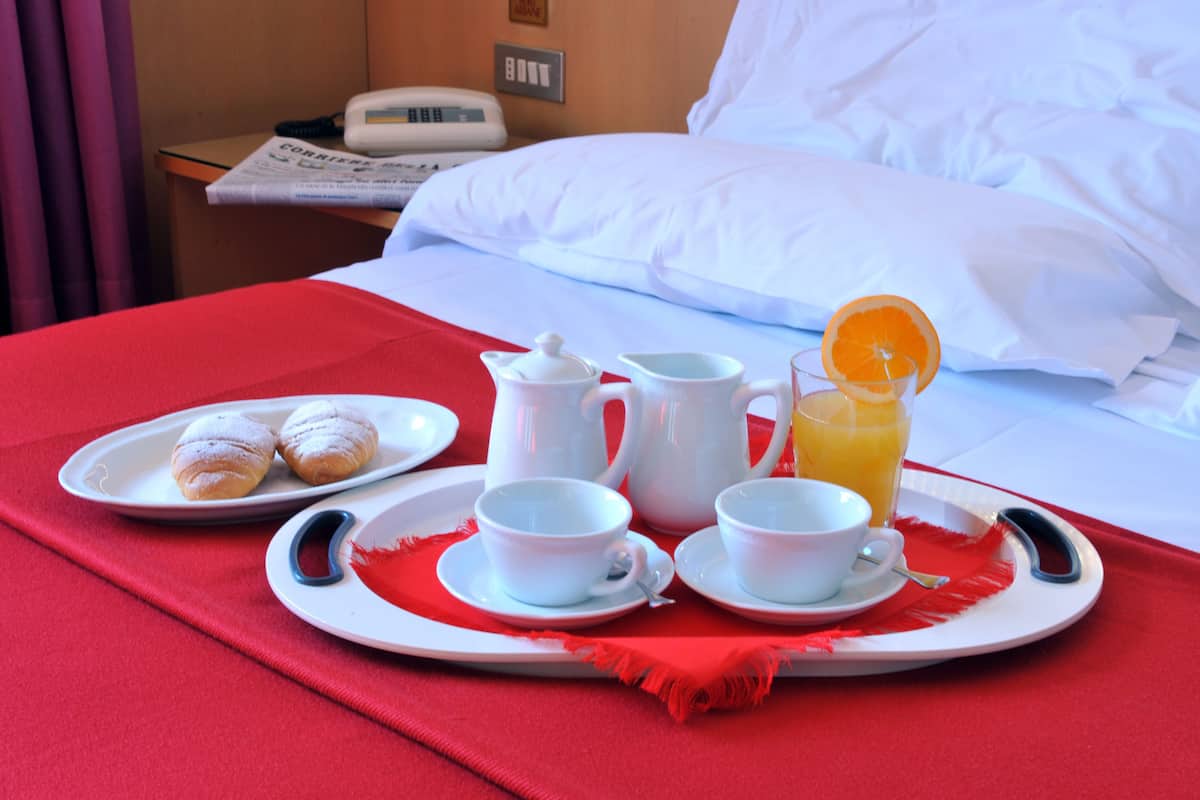 Uma bandeja de café da manhã bem arrumada com doces, xícaras de café, um jarro e um copo de suco de laranja sobre uma toalha de mesa vermelha.