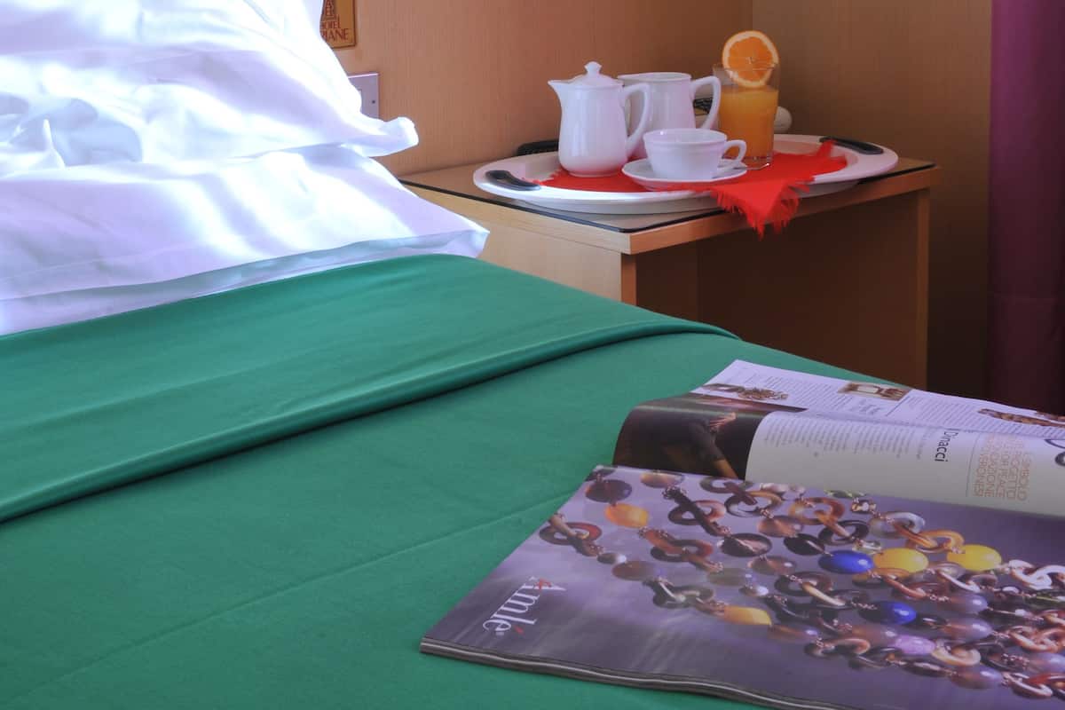 Quarto de hotel com cama bem arrumada, mesa de cabeceira com bandeja de itens de café da manhã e uma revista sobre a cama.