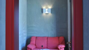 A small room with a red door, a pink sofa, a small table, and a wall-mounted light fixture.
