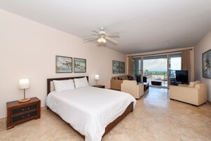Habitación de hotel con una cama grande, ventilador de techo, televisor, sofá y balcón con vistas.
