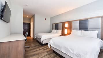 A hotel room with two beds, a desk, a TV, and a wooden floor.