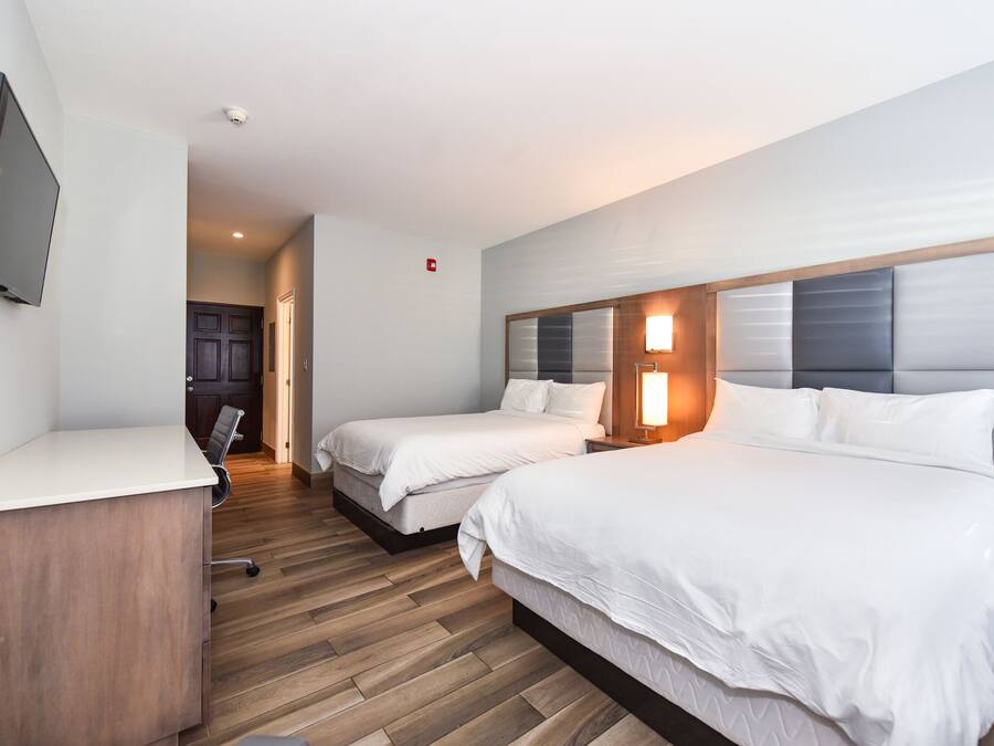 A hotel room with two beds, a desk, a TV, and a wooden floor.