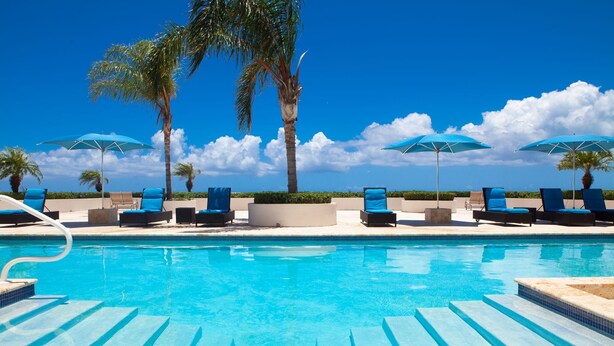 Un espace piscine agrémenté de chaises longues et de parasols, entouré de palmiers.