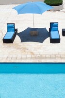 Zona de piscina con dos sillas de descanso, una sombrilla azul y un macetero con plantas.