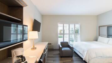 A hotel room with a bed, a TV, a coffee maker, a chair, and a window with blinds.