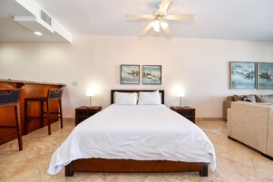 A hotel room with a large bed, a desk with chairs, a sofa, and two wall-mounted paintings.