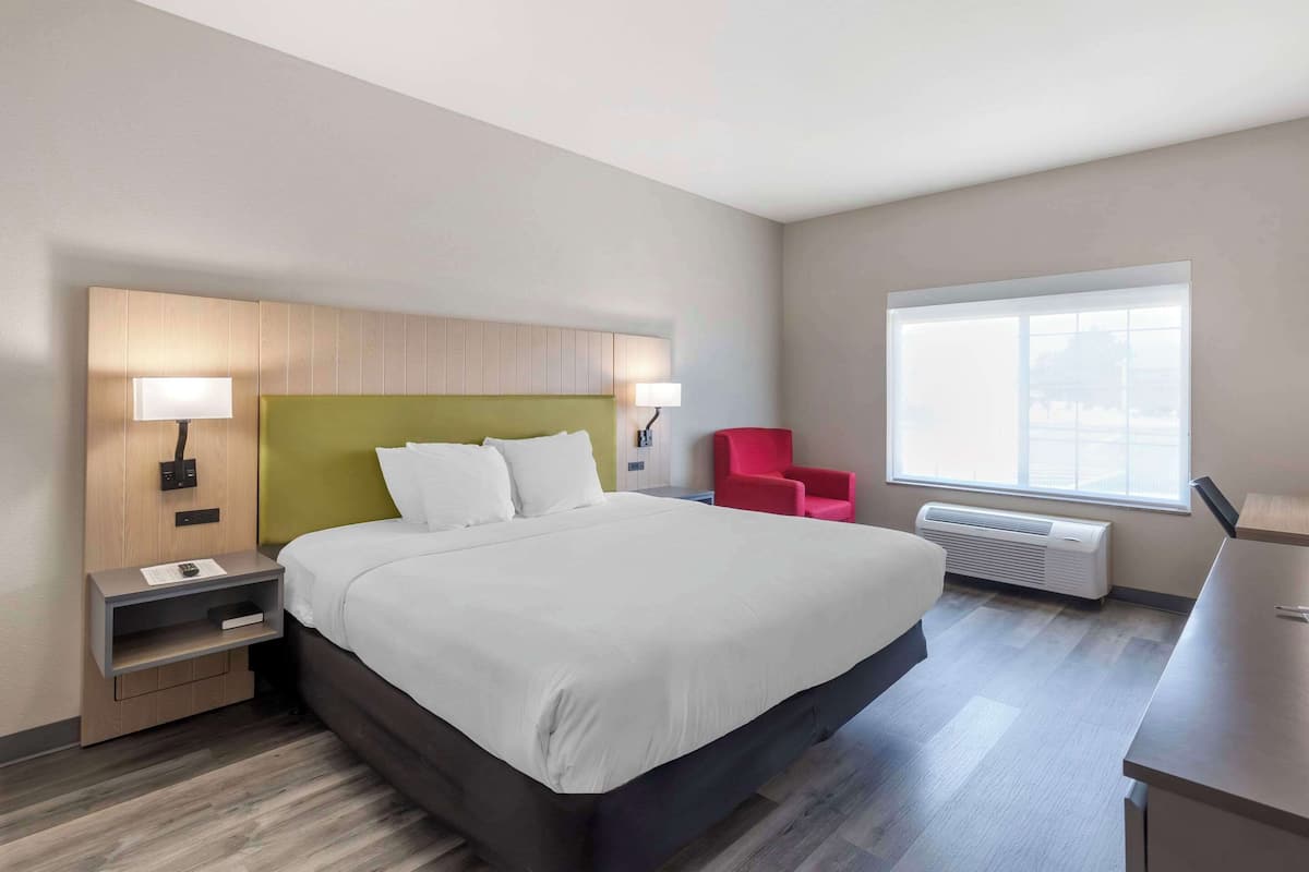A modern hotel room with a large bed, bedside lamps, a red chair, and a window with a view.