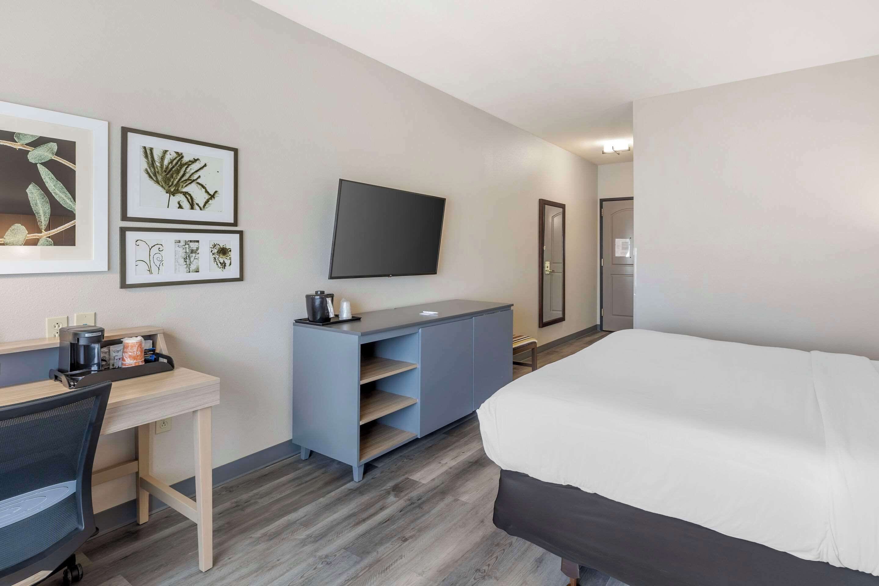 Ein modernes Hotelzimmer mit Bett, Schreibtisch, Stuhl, Fernseher und Kunstwerk an der Wand.