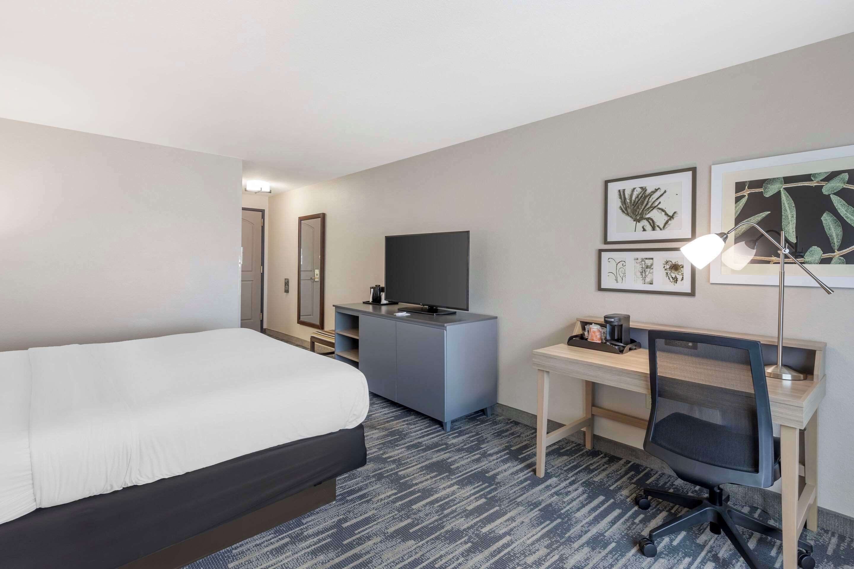A hotel room with a bed, a desk with a computer, a TV, and artwork on the wall.