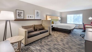 A hotel room with a sofa, a bed, a desk, and a lamp. - Country Inn & Suites by Radisson, St. Peters, MO (St. Charles)