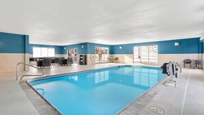 An indoor swimming pool with a blue interior, a seating area with tables and chairs, and a view of the outside through large windows. - Hampton Inn & Suites New Castle (New Castle)